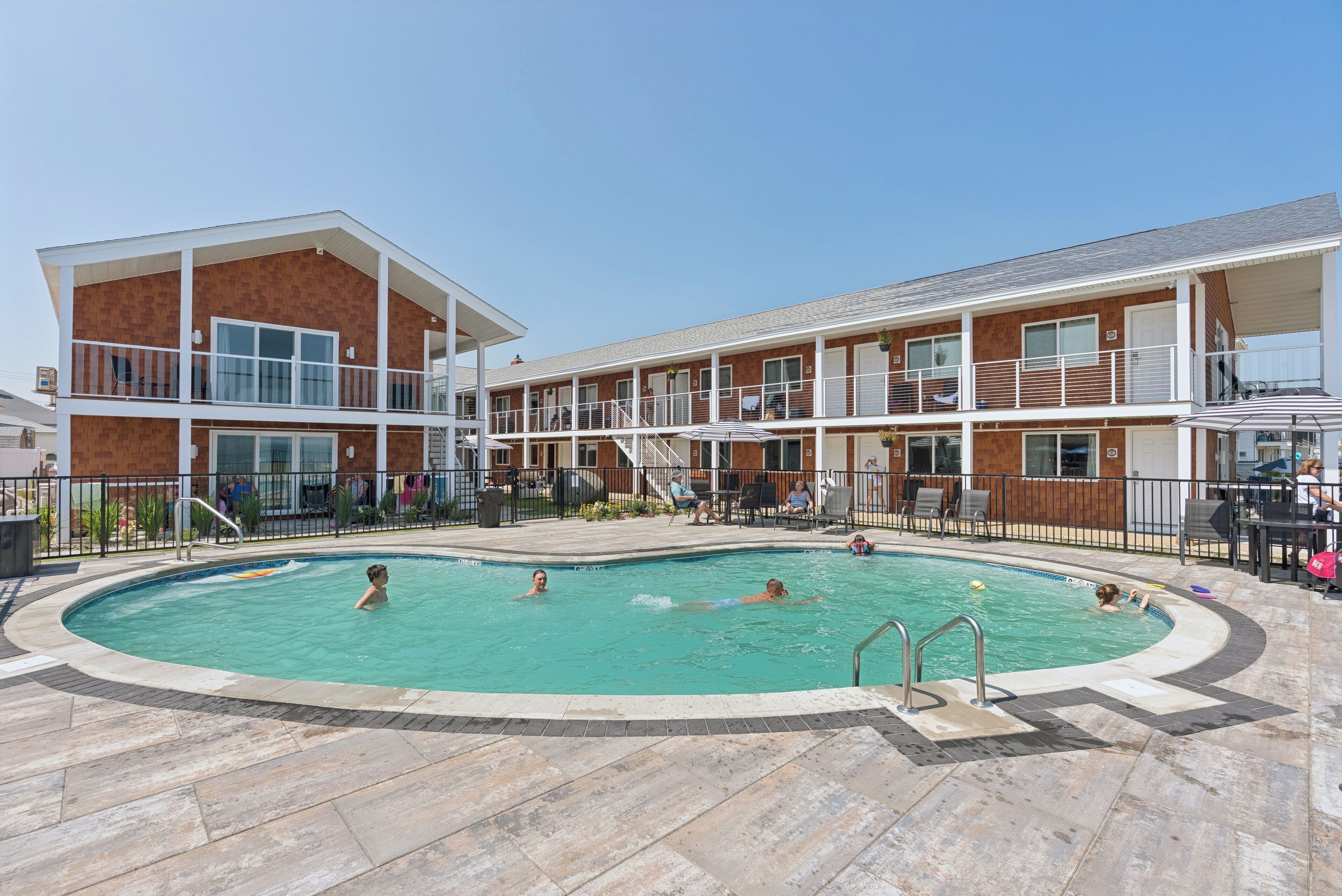 A swimming pool area with a multi-level building, outdoor seating, and a clear sky.