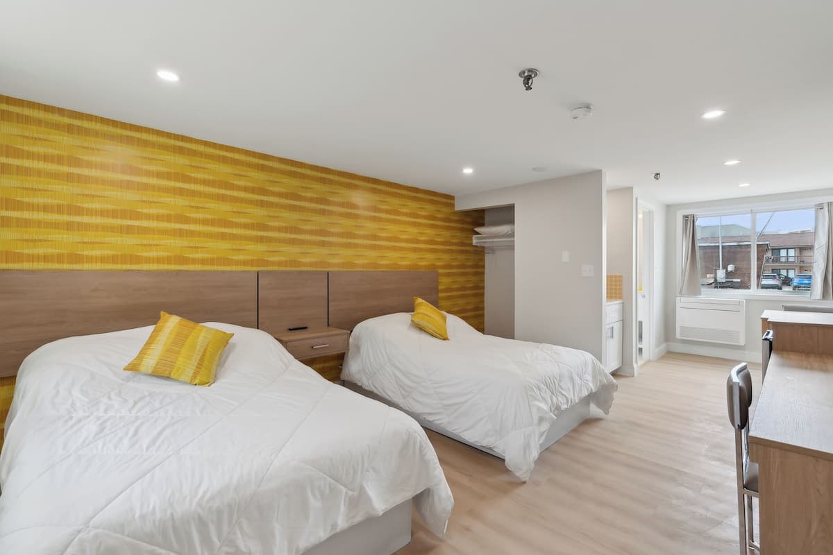 Habitación de hotel con dos camas, cabeceros de madera, un escritorio y una ventana con vistas a edificios.