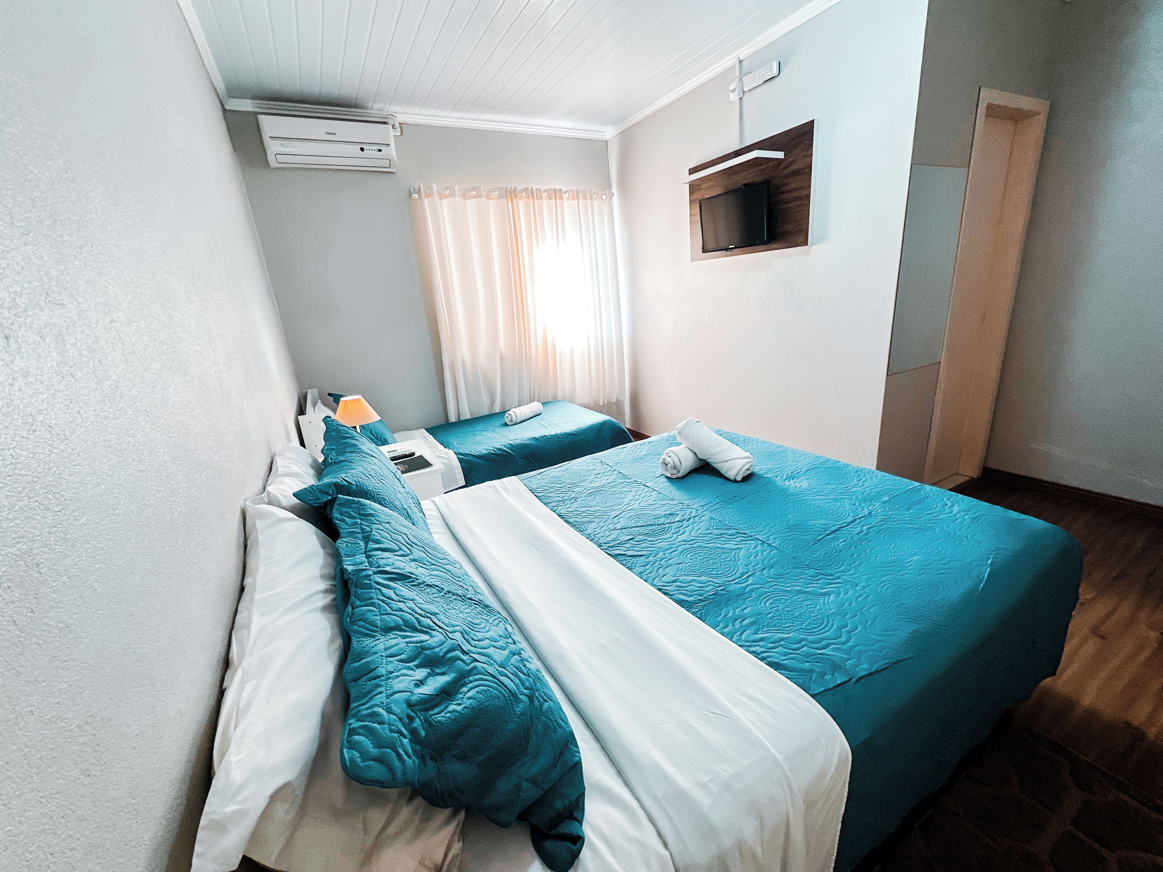 Habitación de hotel con dos camas, un televisor montado en la pared y una ventana con cortinas.