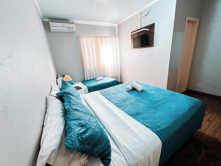 Habitación de hotel con dos camas, un televisor montado en la pared y una ventana con cortinas.