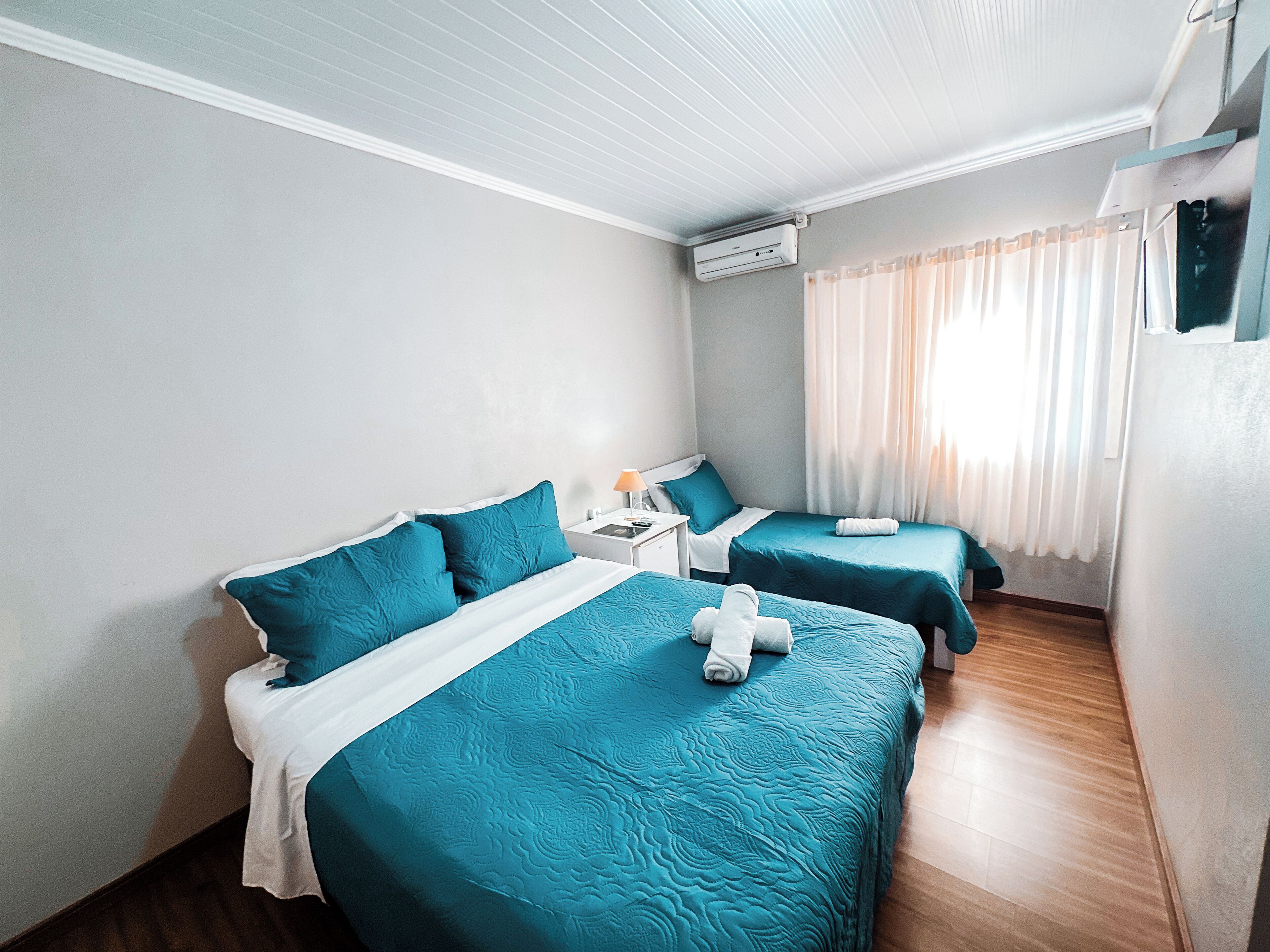 Une chambre d’hôtel avec deux lits, une table de chevet, un appareil de climatisation et une fenêtre avec des rideaux.