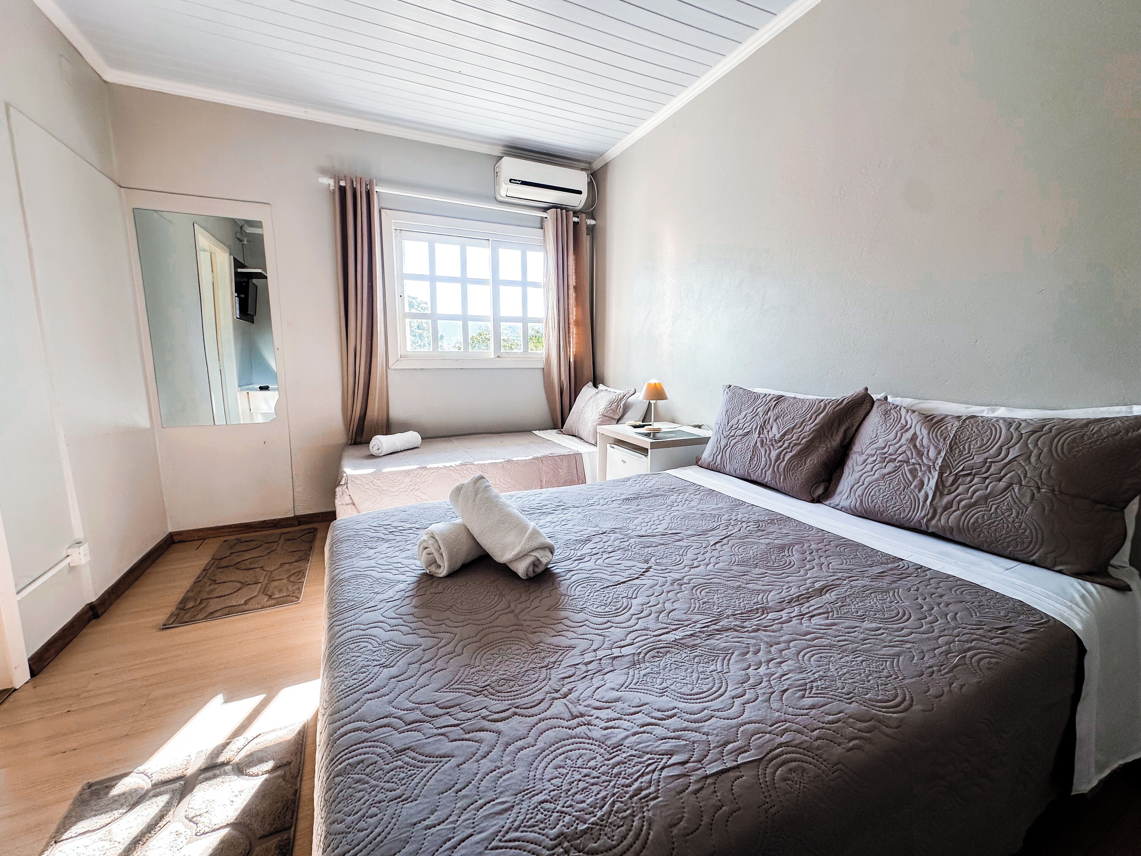 Een hotelkamer met een groot bed, een nachtkastje met lamp, een raam met gordijnen en een airconditioning.