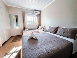 Una habitación de hotel con una cama grande, una mesita de noche con lámpara, una ventana con cortinas y un equipo de aire acondicionado.