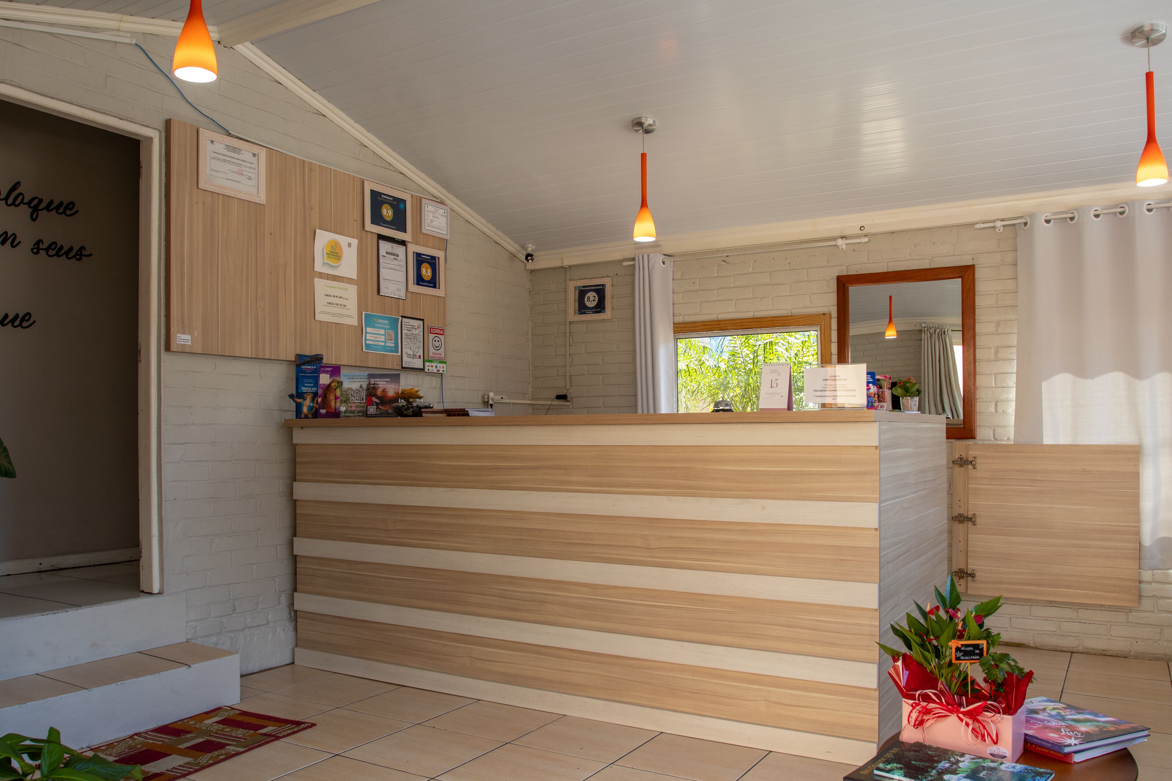 A reception area with a wooden reception desk, a bulletin board with various notices, and a window with a view of greenery outside.