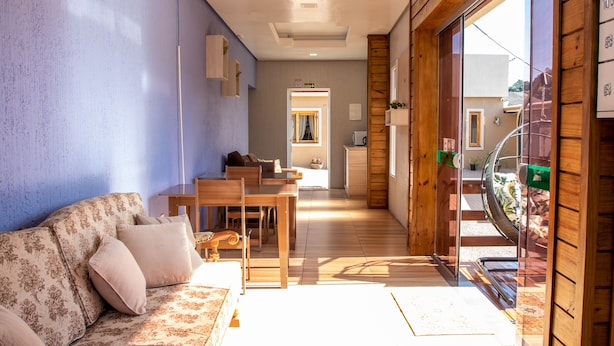 A modern living room with a sofa, coffee table, and dining area. There is a sliding glass door leading to a balcony with a view of the outside. - Pousada Boschetti (Gramado)