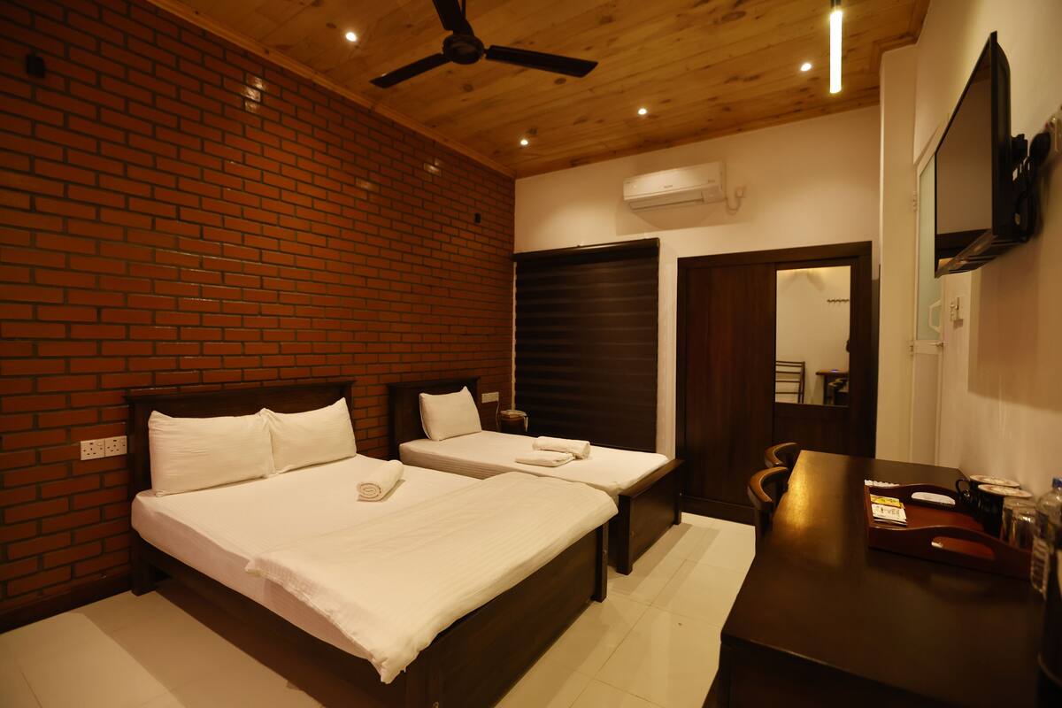 A hotel room with two beds, a wooden ceiling, brick walls, a flat-screen TV, and a desk with a chair.