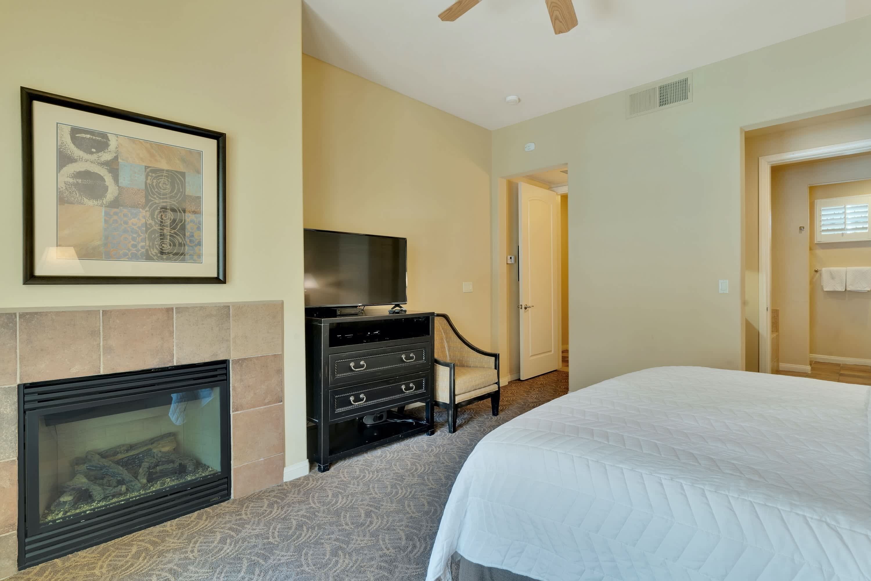 A bedroom with a fireplace, a television, a bed, and a door leading to another room.