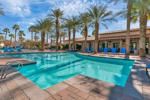 Una piscina con sillas reclinables azules y palmeras.