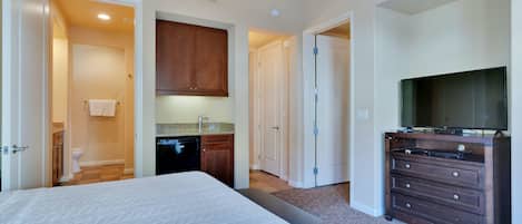 A hotel room with a bed, a dresser, a television, and a kitchenette.
