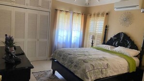 A bedroom with a bed, a desk, a wardrobe, and a decorative wall piece. - Island Style Villa in Richmond Estate Palms (St. Ann Parish)