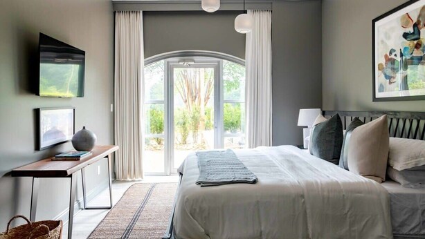 A modern bedroom with a large bed, a desk, a television, and a view of the outdoors. - Church St Collection - 109 Full House (Fairhope)