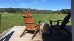 Une terrasse en bois, dotée de chaises Adirondack, qui offre une vue sur un champ verdoyant et des collines lointaines.