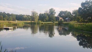 Un lac paisible avec un quai, entouré d’une végétation luxuriante et un petit bâtiment en arrière-plan.