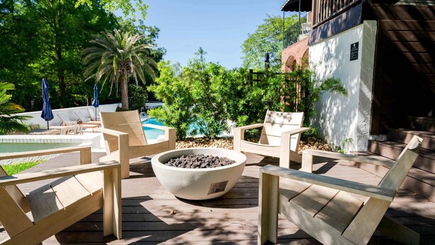 Eine Holzterrasse mit Liegestühlen, einer Feuerstelle und einem Pool im Hintergrund.