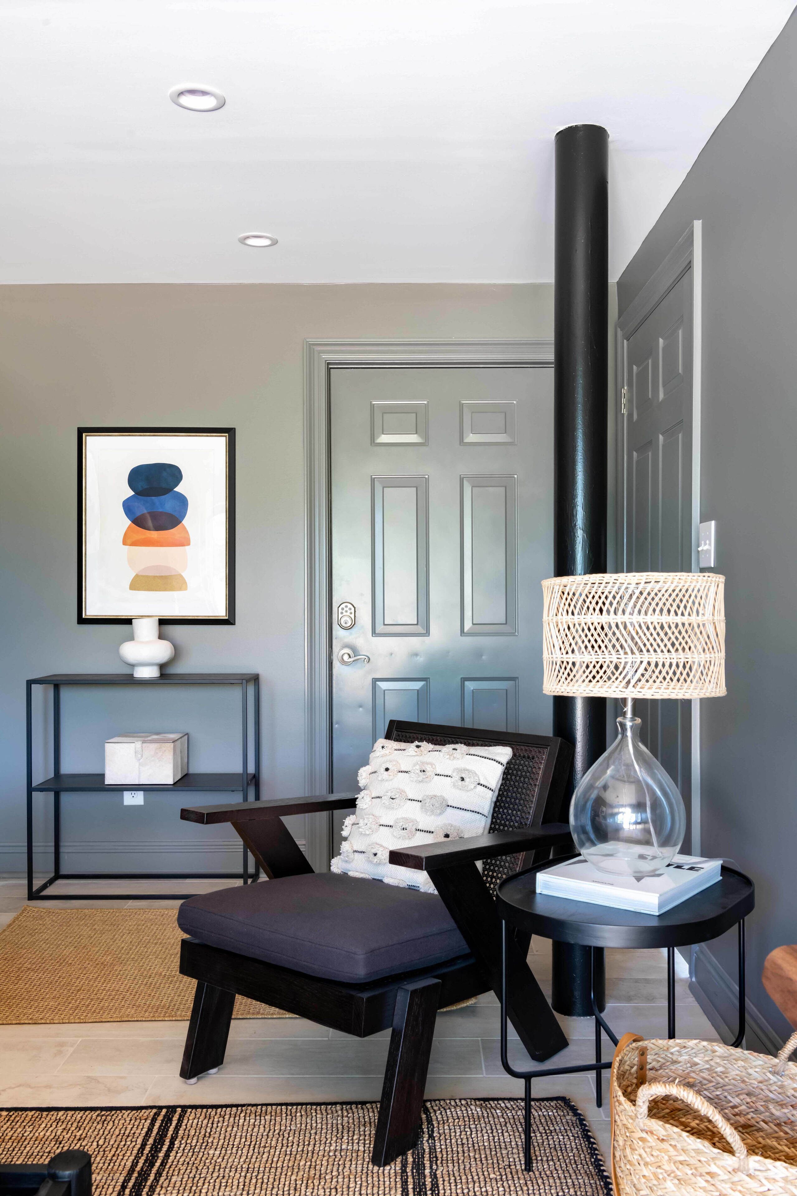 A modern living room with a dark leather armchair, a small side table with a lamp, a framed abstract artwork, and a door with a frosted glass panel.