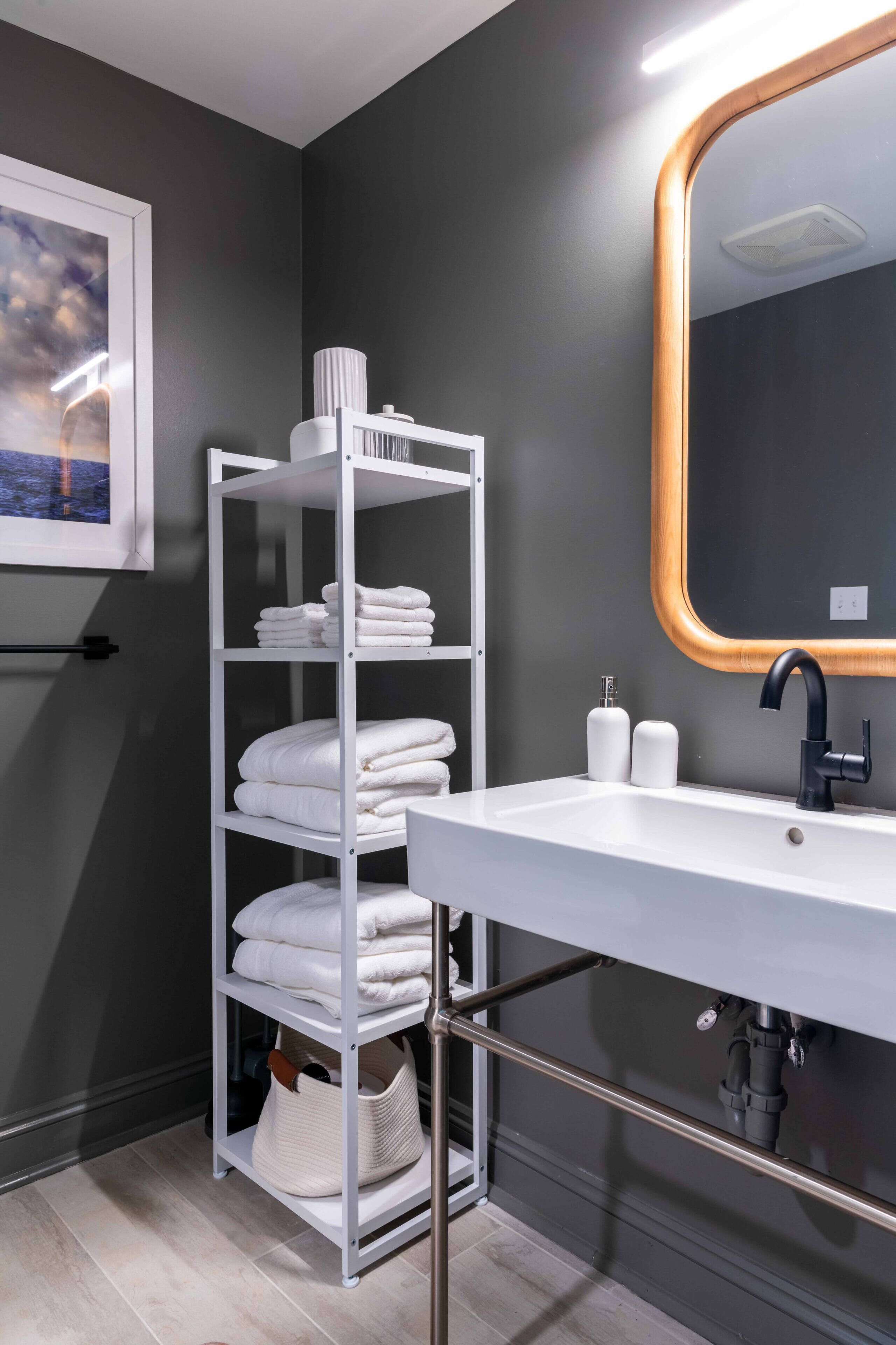 A modern bathroom with a white sink, a mirror with a wooden frame, and a towel rack with neatly folded towels.