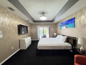 A hotel room with a bed, a television, a painting, and a view of the outdoors.