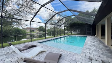 A covered outdoor swimming pool with lounge chairs and a view of a lake.