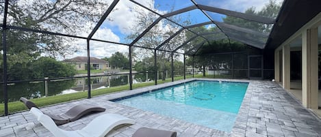 A covered outdoor swimming pool with lounge chairs and a view of a lake.