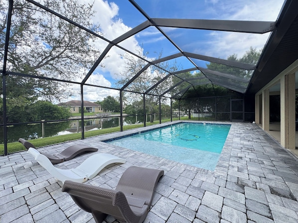 A covered outdoor swimming pool with lounge chairs and a view of a lake.