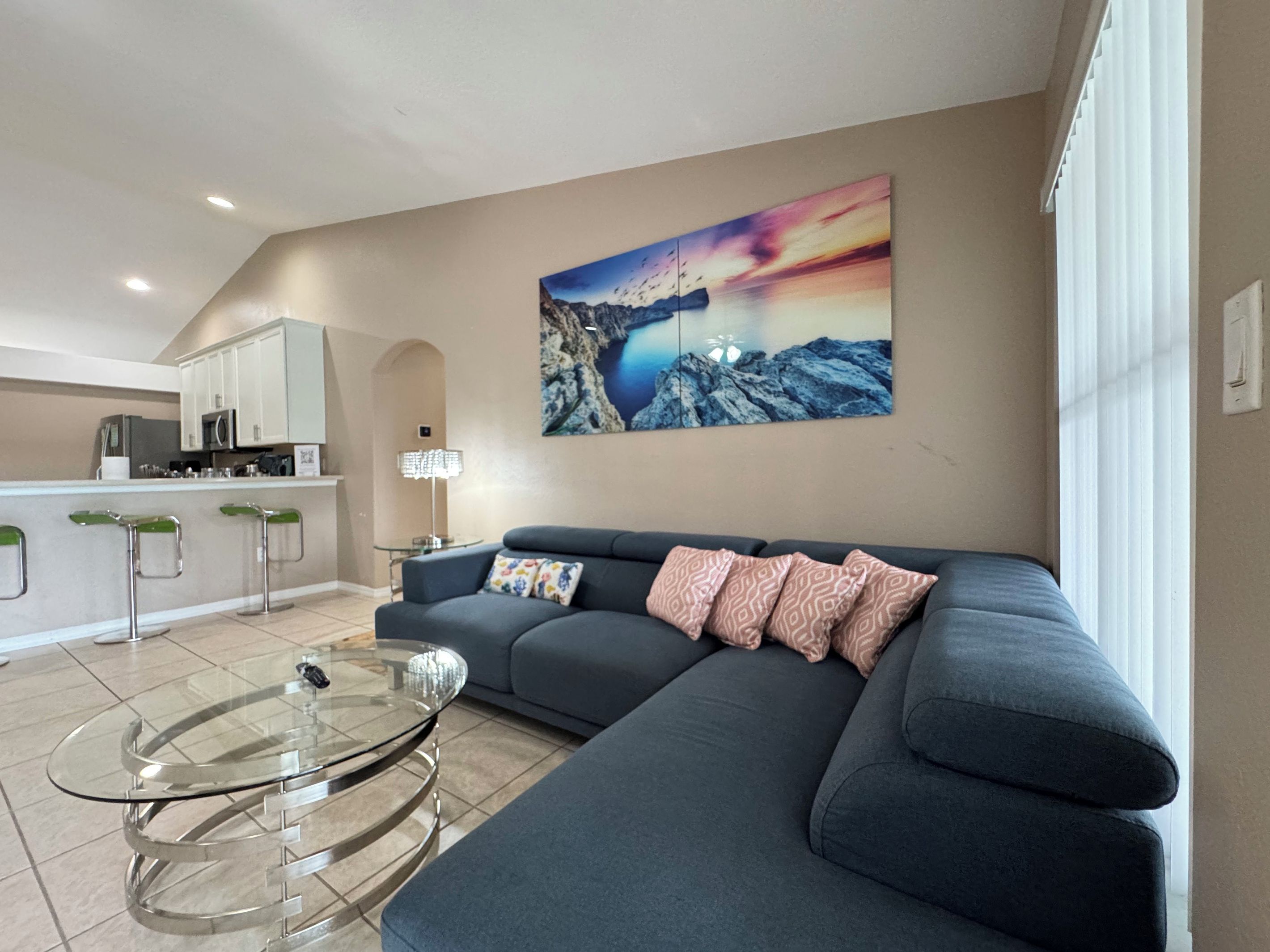 A modern living room with a sofa, a glass coffee table, and a kitchen area in the background.