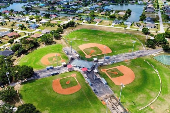 An aerial view of a baseball field with multiple diamonds, surrounded by residential houses and a body of water.