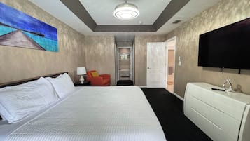 A hotel room with a large bed, a TV, a desk, and a painting on the wall.