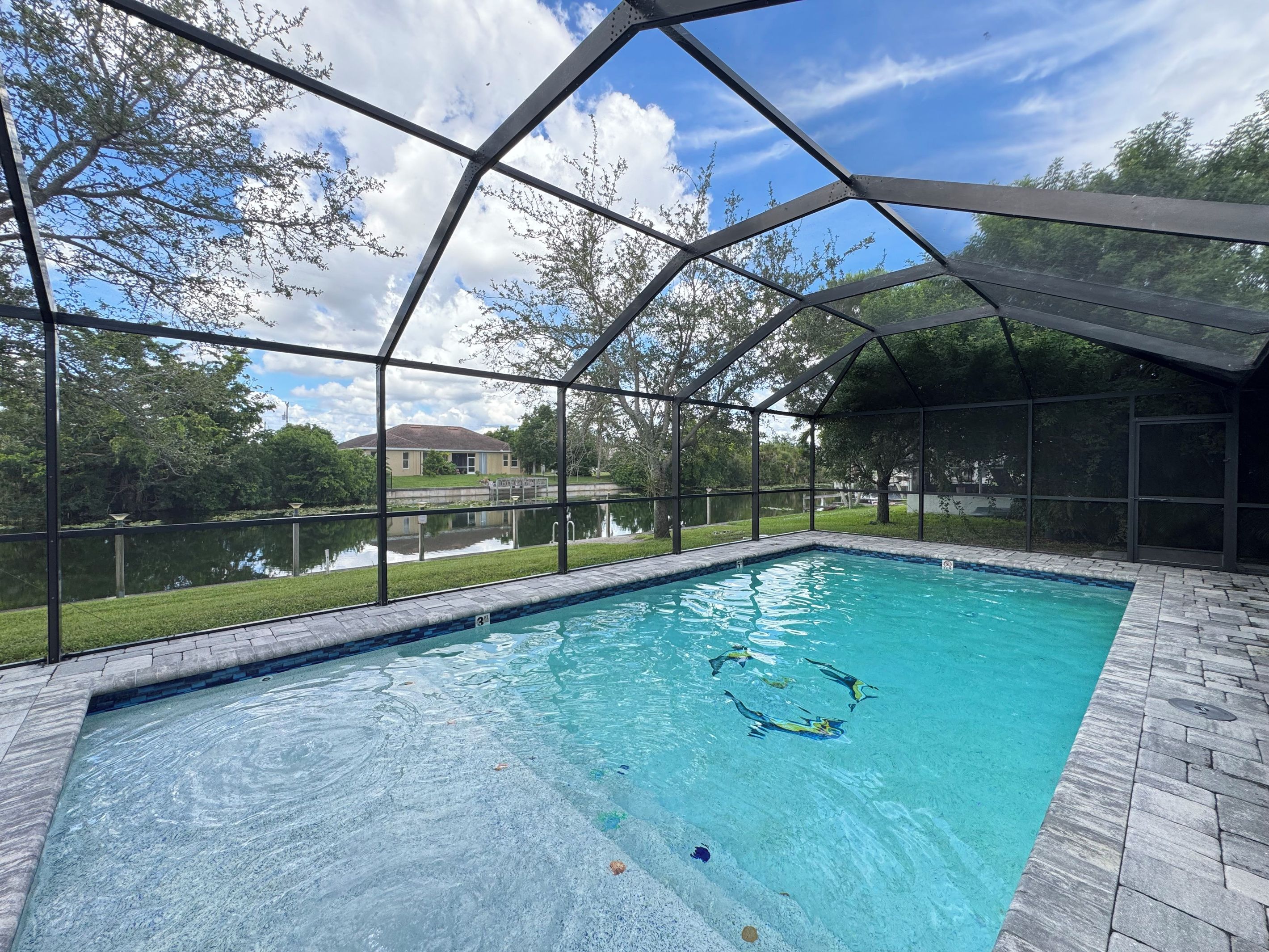 Piscina com vista clara para uma casa e um corpo de água ao fundo.