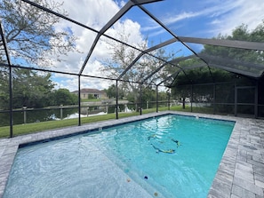 A swimming pool with a clear view of a house and a body of water in the background.