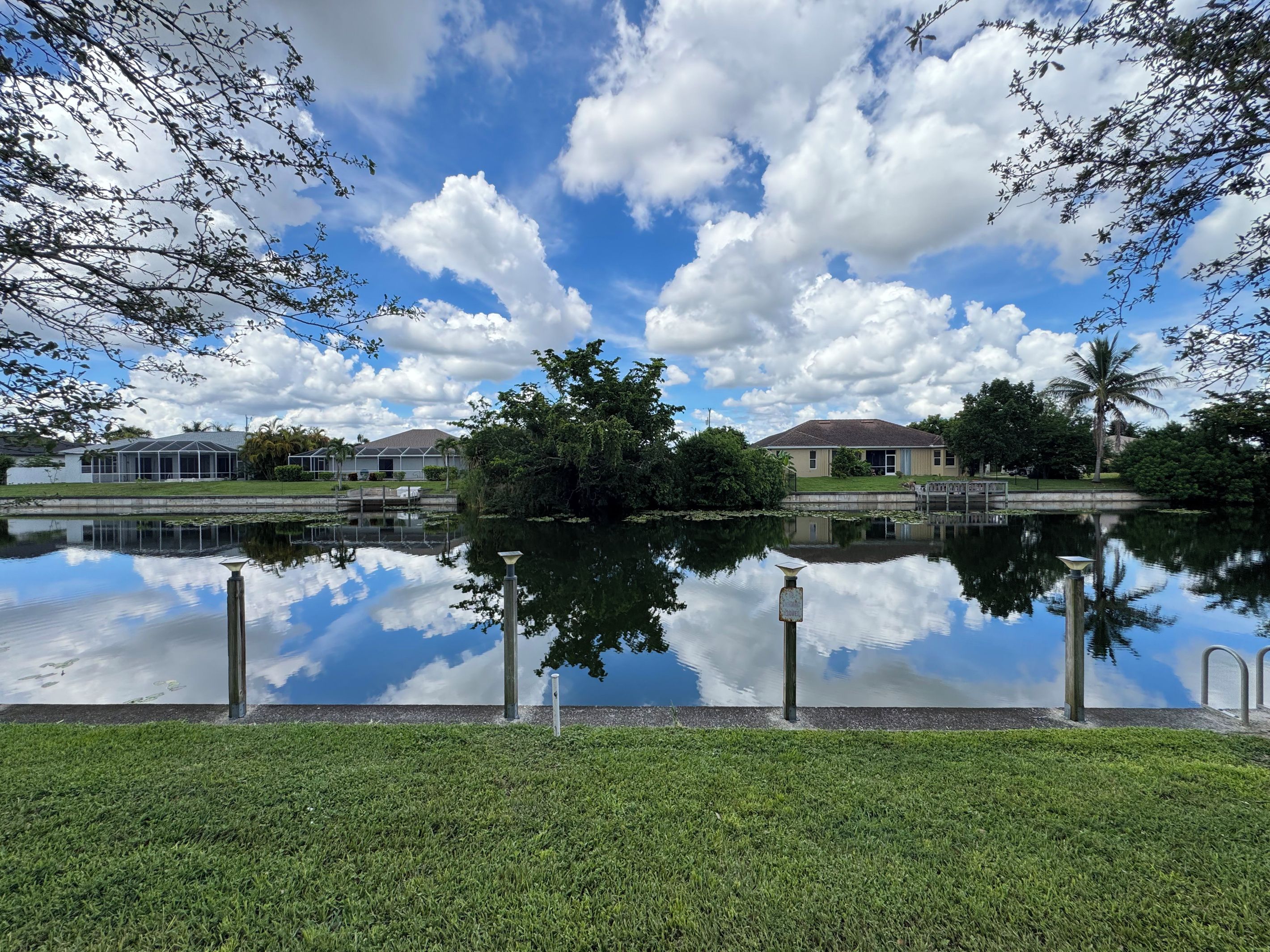 A tranquil lakeside view with a clear sky, calm water reflecting the surroundings, and a grassy foreground.