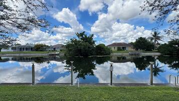 A tranquil lakeside view with a clear sky, calm water reflecting the surroundings, and a grassy foreground.
