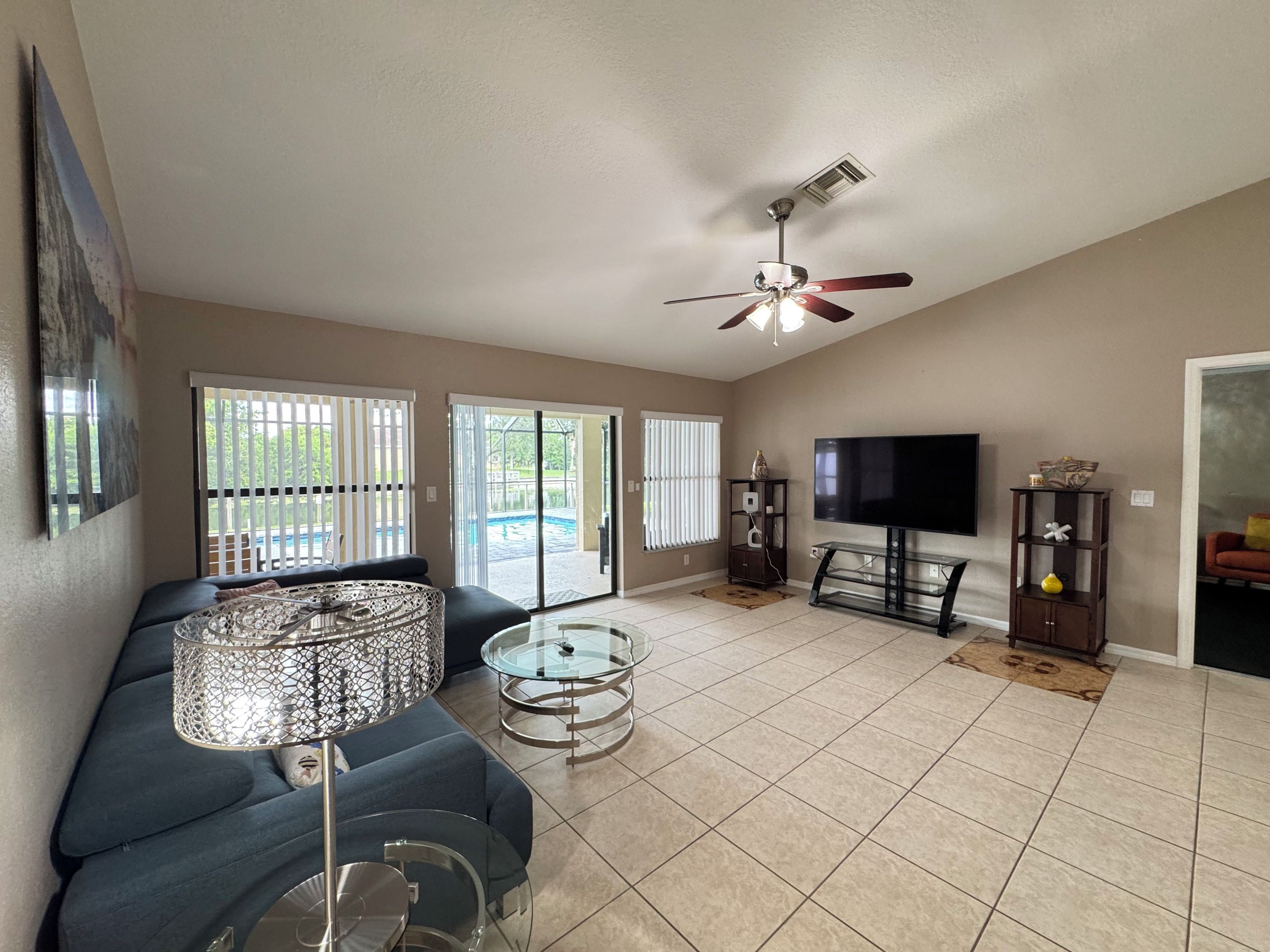 A living room with a sofa, a glass coffee table, a TV, and a ceiling fan.