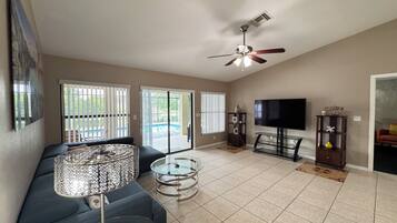 A living room with a sofa, a glass coffee table, a TV, and a ceiling fan.