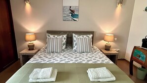 Una cama doble con colcha de estampado de hojas, dos almohadas, dos lámparas de noche y un cuadro enmarcado en la pared.