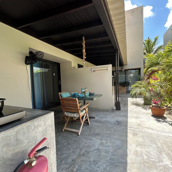 An outdoor patio with a table and chairs, a fire extinguisher, and a potted plant.