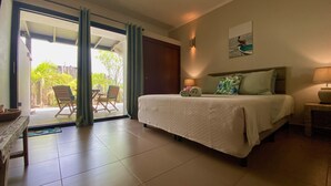Habitación de hotel con cama, mesita de noche, lámpara, ventana con cortinas y vistas al exterior.