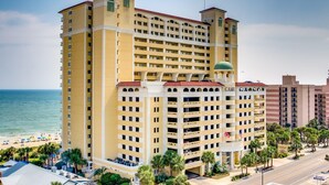A multi-story hotel with a central courtyard, a pool area, and a beach view.