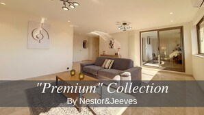 A modern living room with a sofa, coffee table, and decorative items. There is a large mirror and a ceiling light fixture. - N&J - BELLE ETOILE- Central - Premium (Niza)
