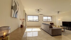 A spacious living room with a grey sofa, a TV, and a large window offering a city view. - N&J - BELLE ETOILE- Central - Premium (Niza)