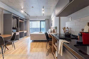 Een moderne hotelkamer met een bed, kitchenette, eethoek en inloopkast.