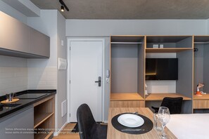 Una habitación de hotel moderna con área de cocina, una mesa de comedor para dos personas y estantes empotrados.