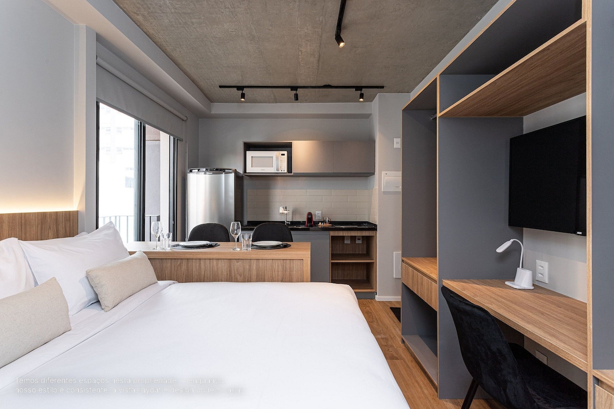 A hotel room with a bed, a desk, a TV, a microwave, and a kitchenette.