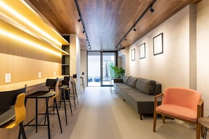 A modern interior with a long counter, bar stools, a sofa, and a pink chair.