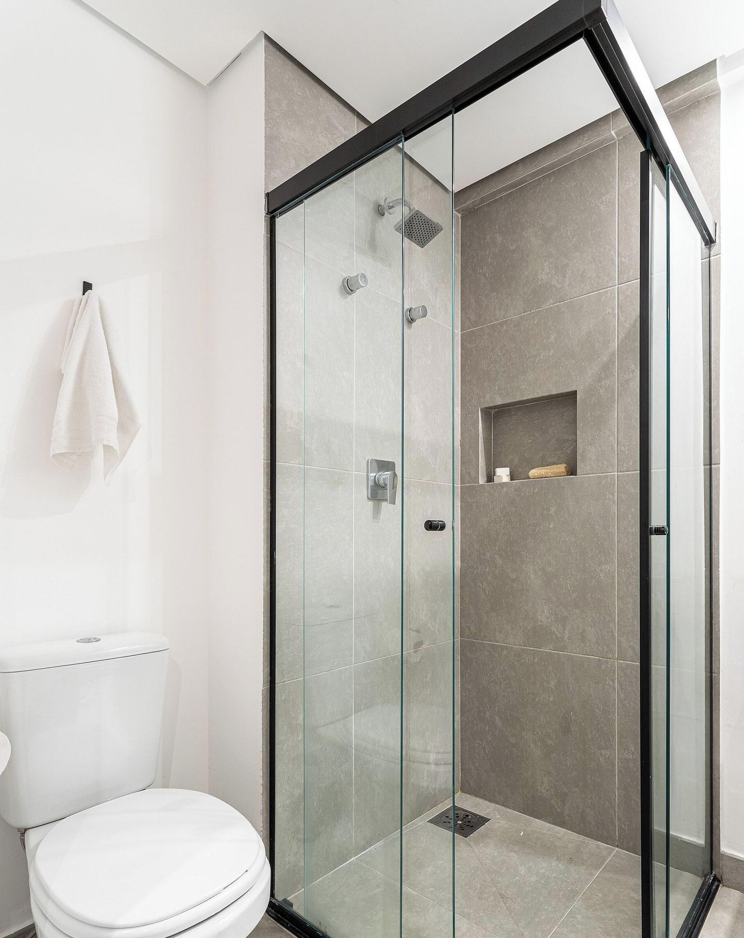 A modern bathroom with a glass-enclosed shower, a toilet, and a towel hanging on the wall.