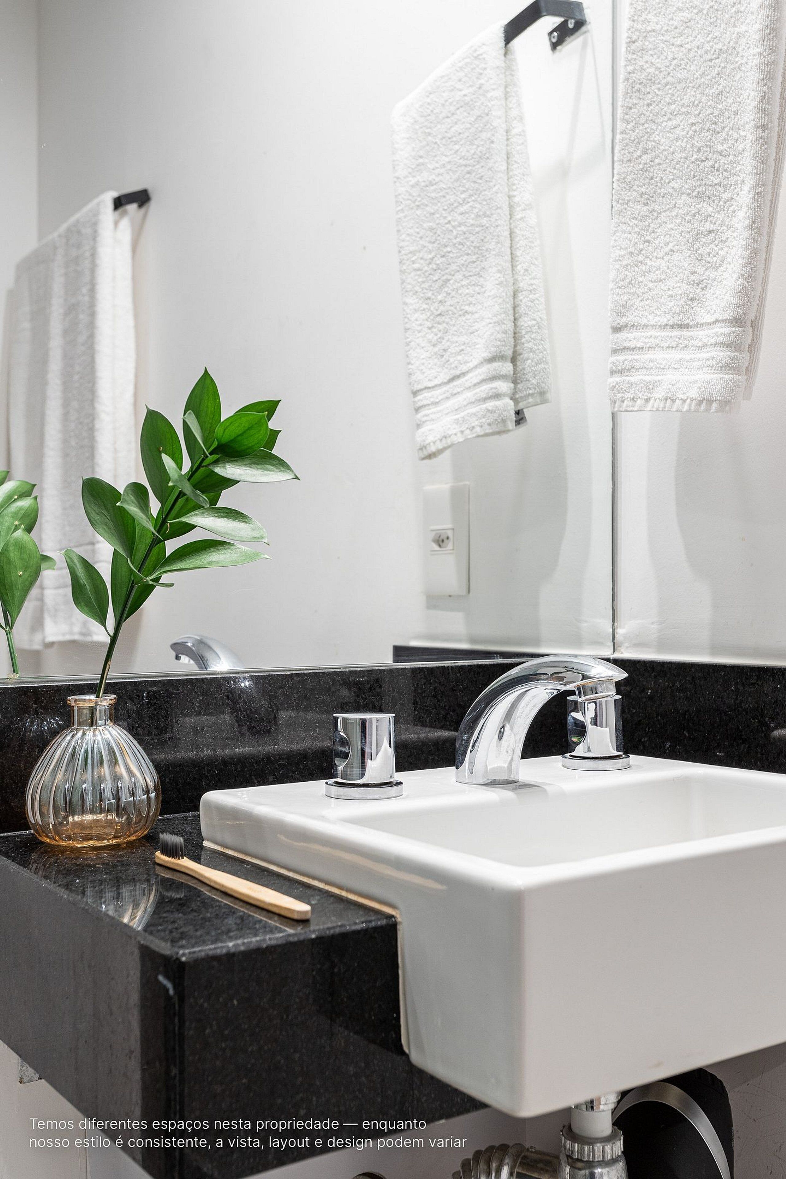 A bathroom with a white sink, black countertop, and a mirror reflecting a towel.