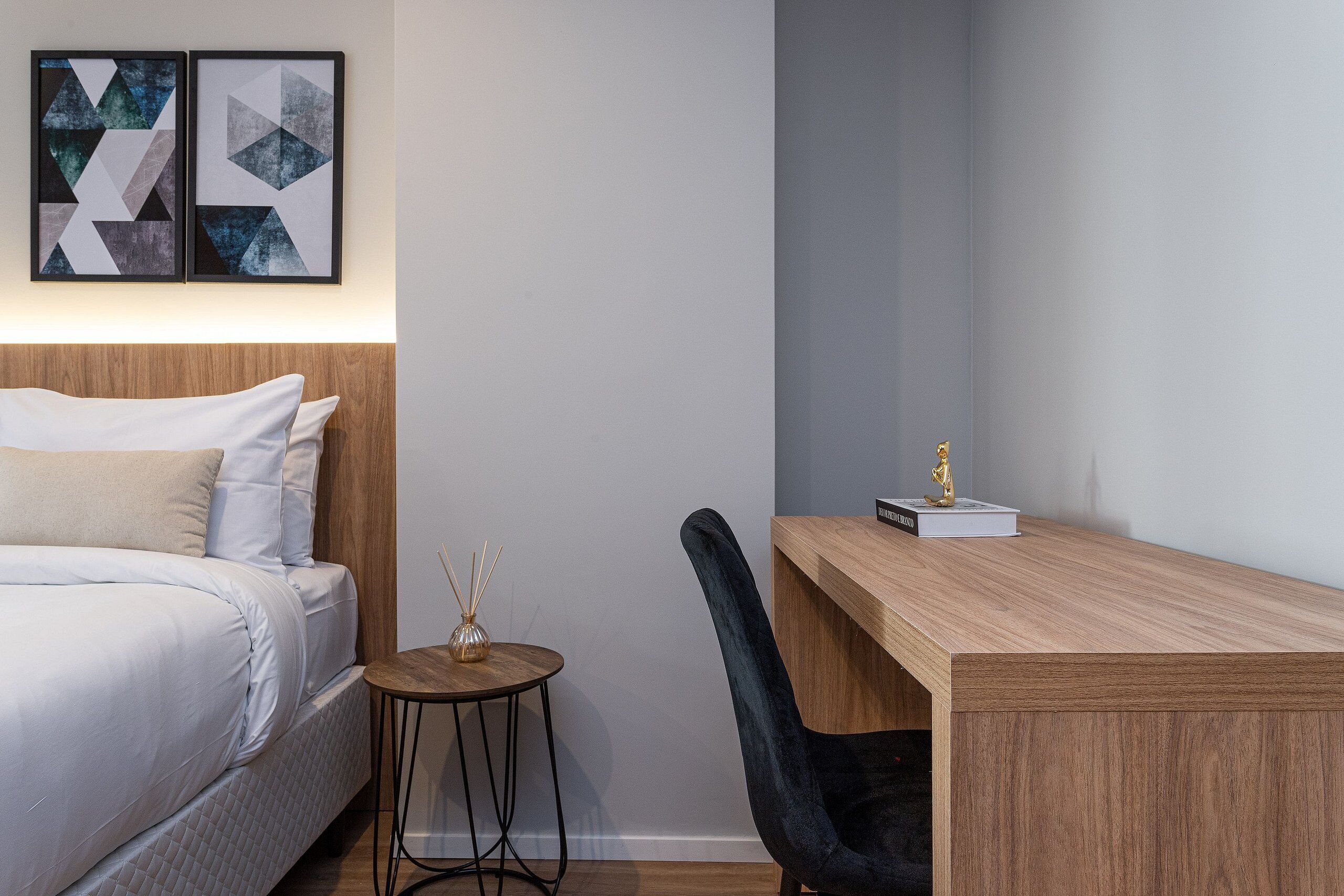 Una habitación de hotel moderna con una cama, un escritorio y una silla. Hay dos obras de arte enmarcadas en la pared sobre la cama.