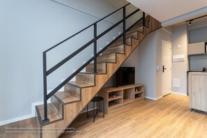 A modern staircase with wooden steps and black metal railings, leading to a living area with a flat-screen TV and wooden furniture.
