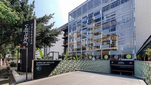 A modern building with a glass facade, a sign for 'Jardim Shopping,' and a 'Saída de Veículos Sentido Proibido' sign. - Next Paulista by Viva - Apartamentos completos ao lado da Av Paulista e MASP (São Paulo)