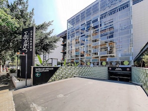 A modern building with a glass facade, a sign for 'Jardim Shopping,' and a 'Saída de Veículos Sentido Proibido' sign.