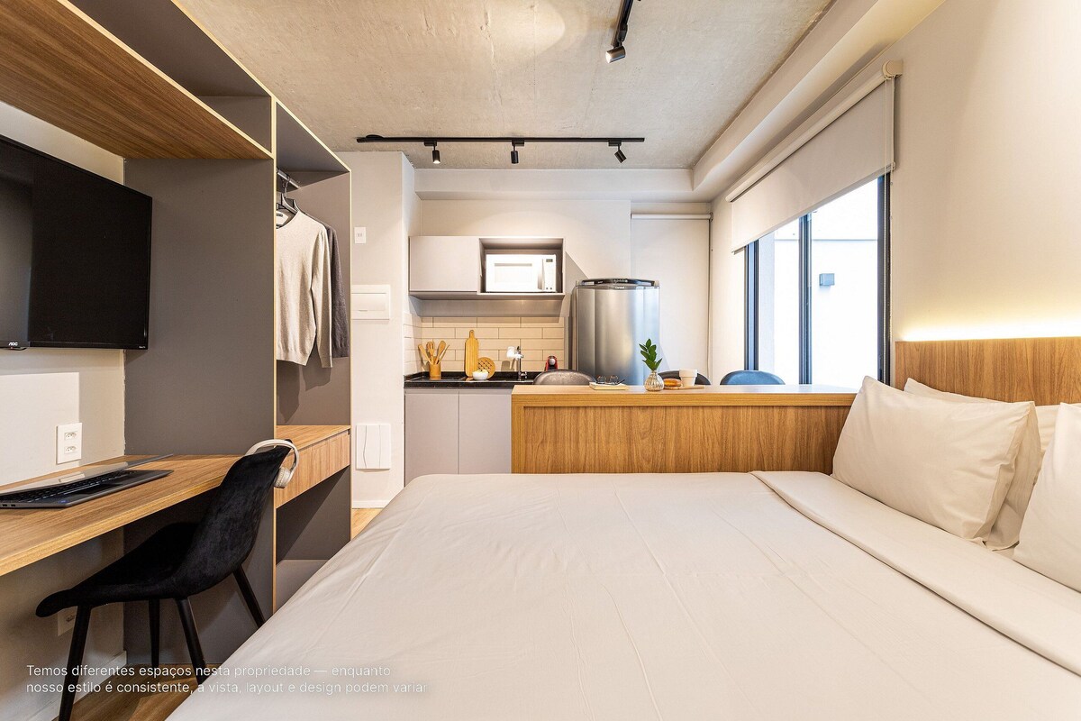 A modern hotel room with a wooden desk, black chair, and a bed with white bedding.